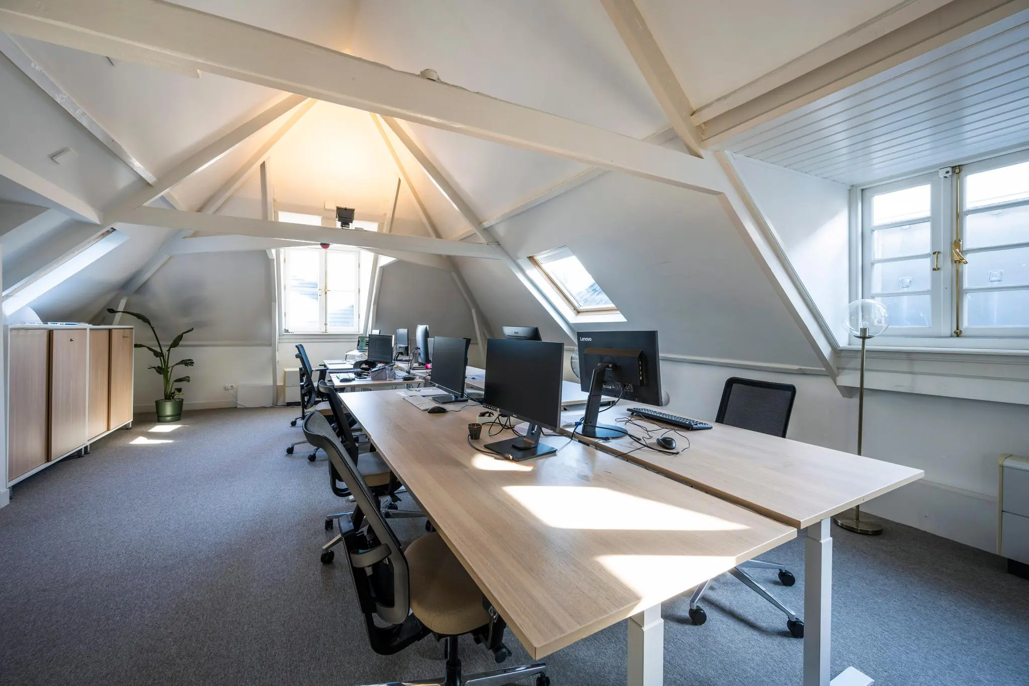 Modern kantoor op zolderverdieping aan de Prof. Tulpstraat met bureaus, computers en natuurlijk licht via schuine dakramen.